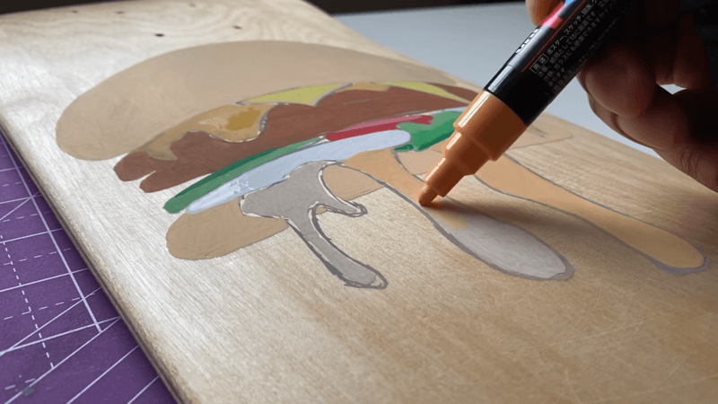 hand painting a hamburger design on a skateboard deck