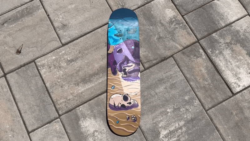 skateboard deck with purple octopus and human skull design laying on the pavement